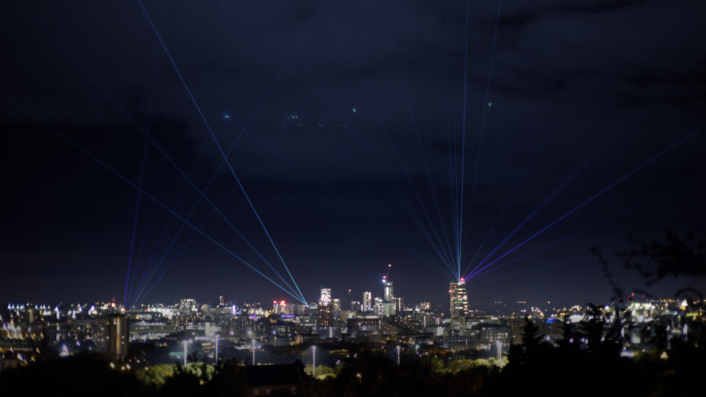 The Leeds skyline at night with laser beams emanated from several rooftops